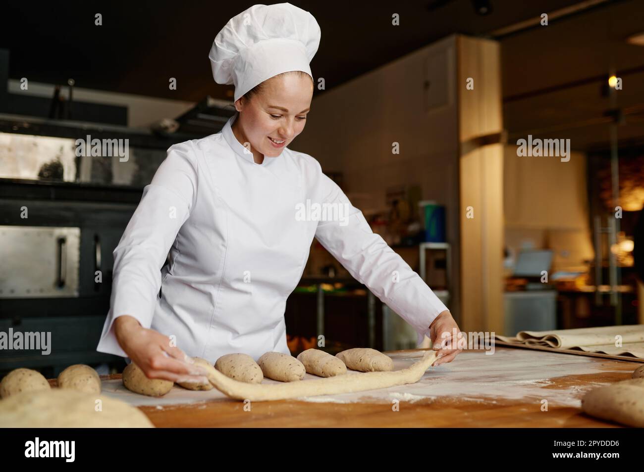 Junge Bäckerin, die in einer Bäckerei arbeitet und Baguettes aus rohem Teig bildet Stockfoto
