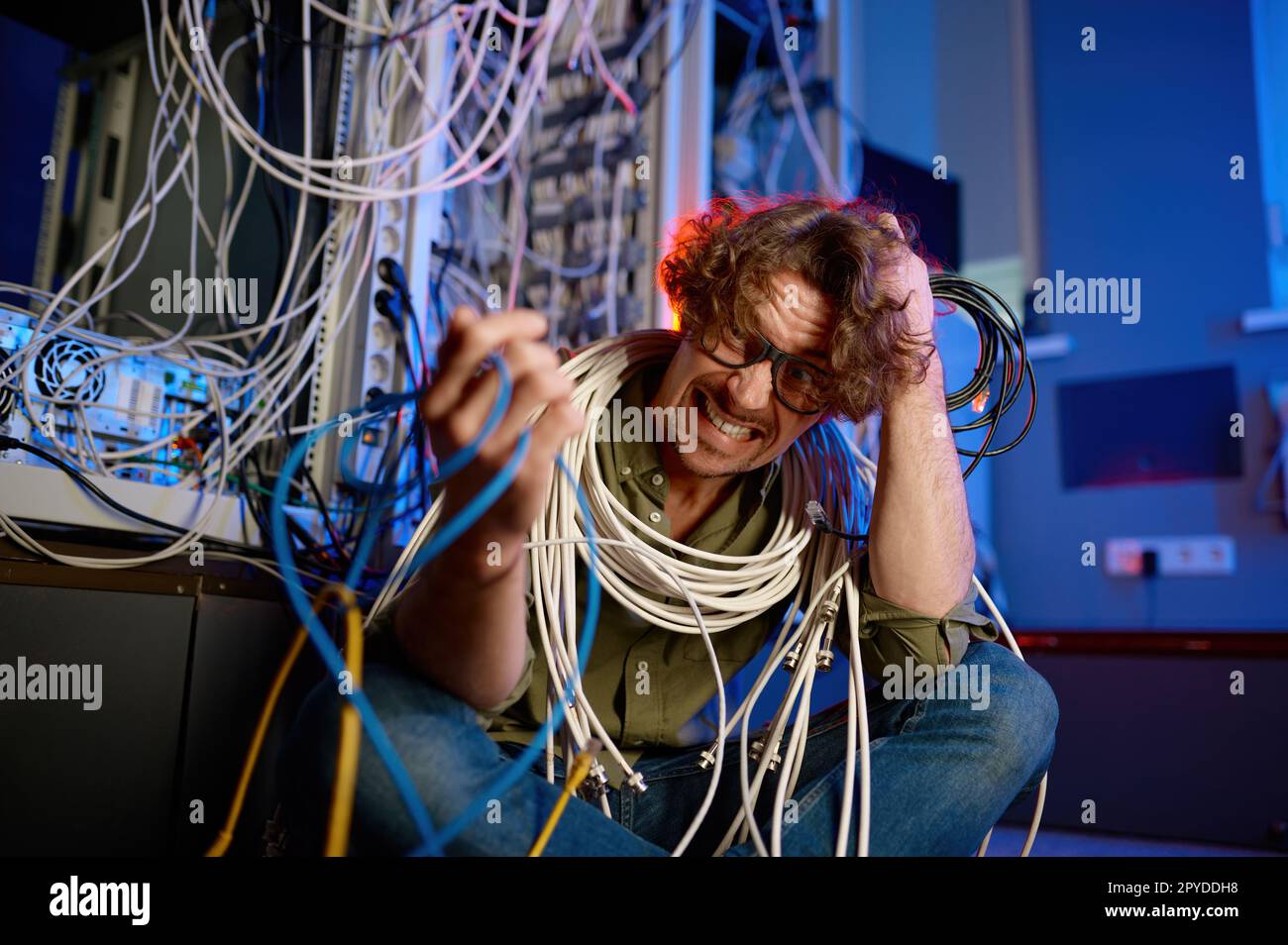 Verrückter, verrückter Computeringenieur, der in Drähte und Kabel im Serverraum eingewickelt ist Stockfoto
