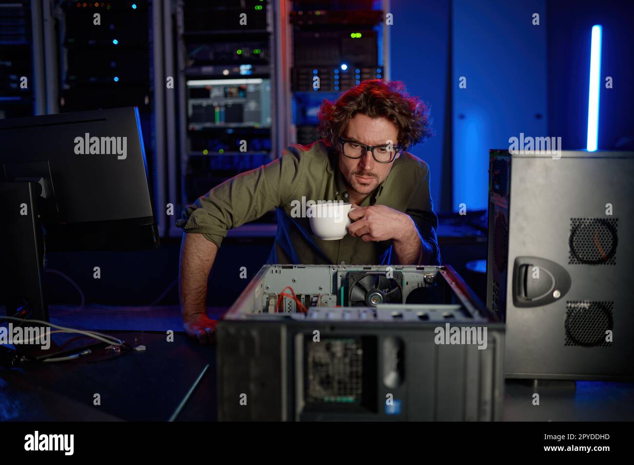 Techniker mit einer Tasse Kaffee, der sich die zerlegte Computersystemeinheit ansieht Stockfoto