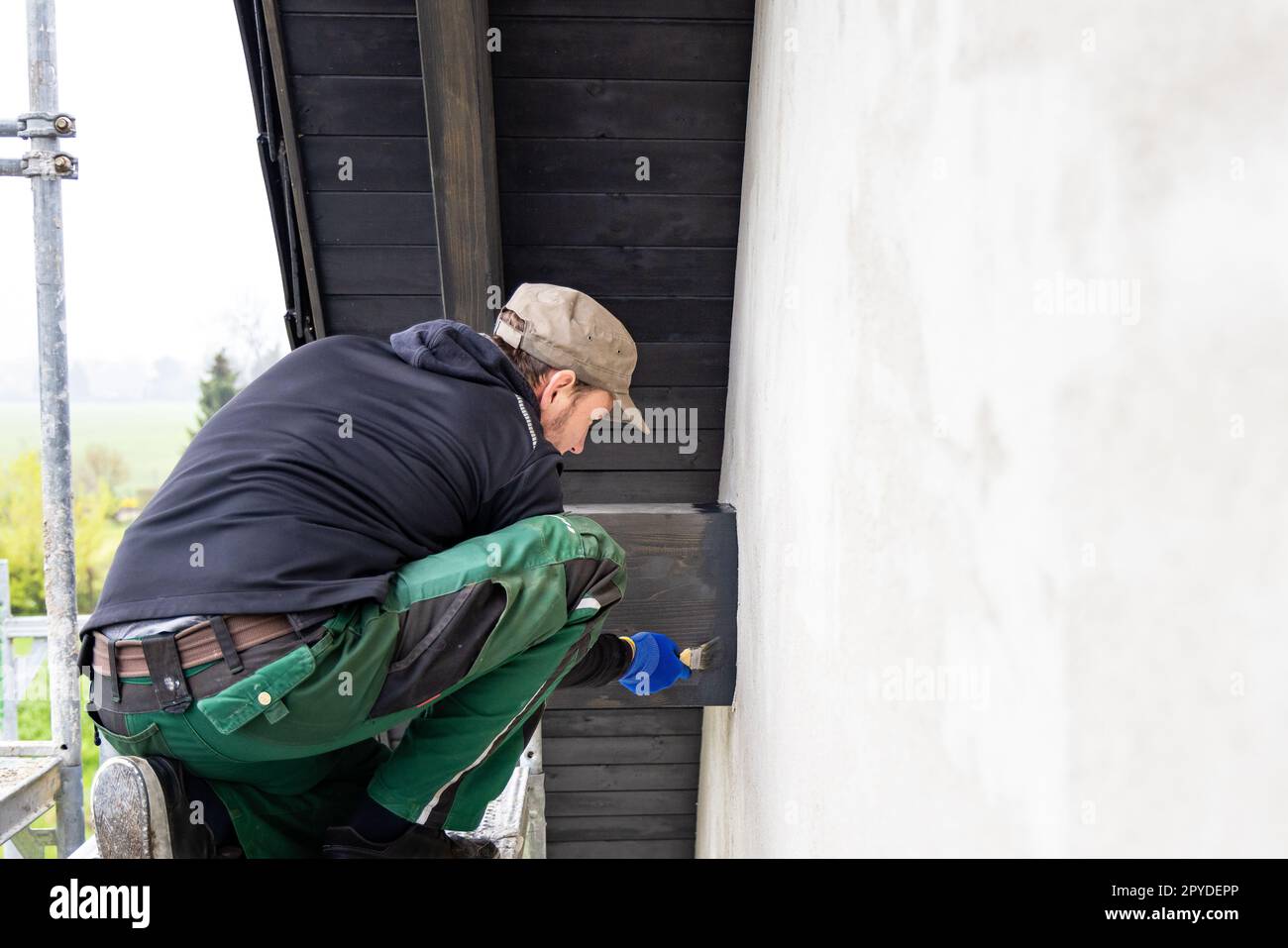 Handwerker, der Holzflecken mit einem Pinsel auf einen Dachbalken eines Hauses aufträgt Stockfoto