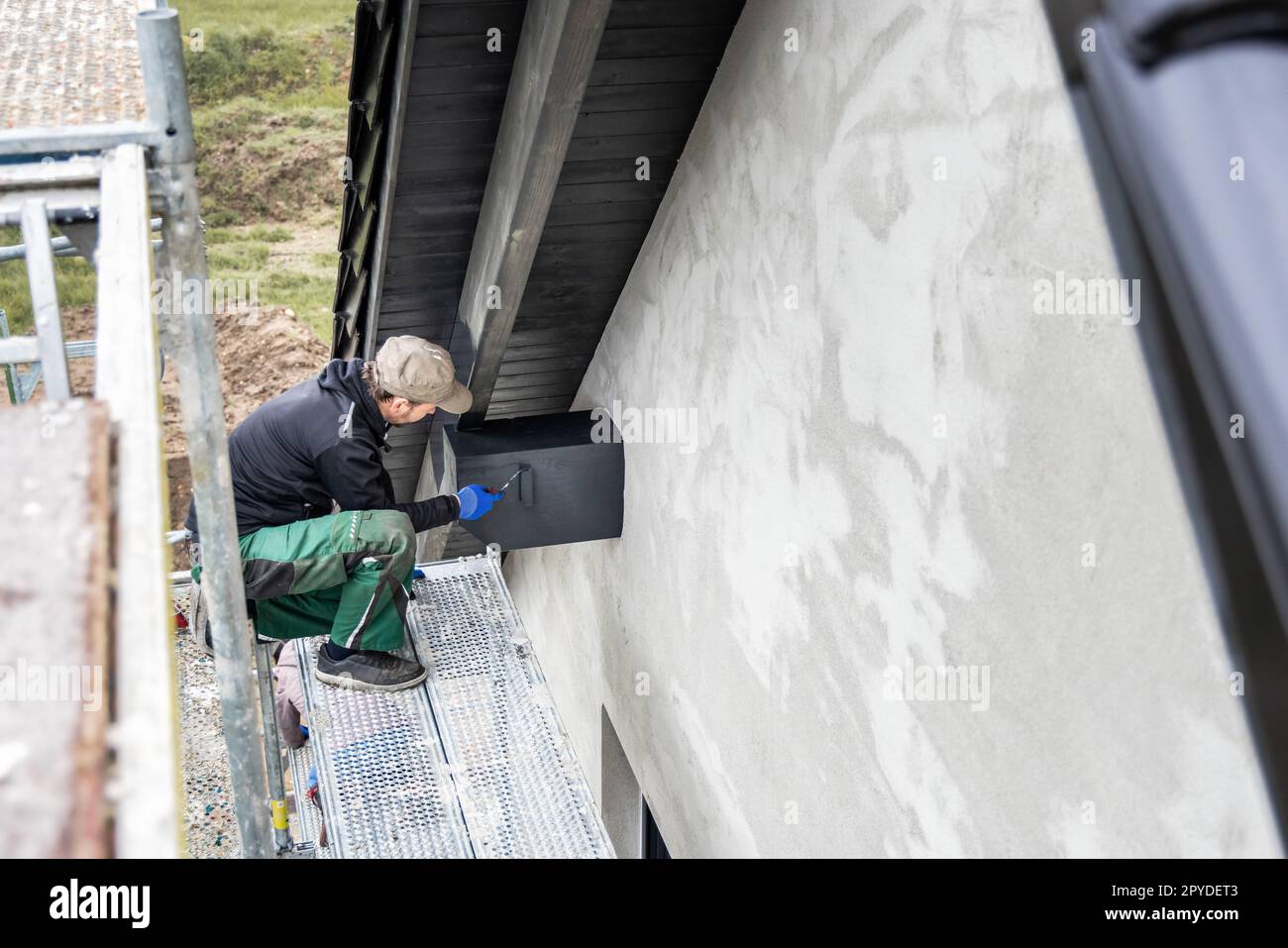 Handwerker, der Holzbeize auf einen Dachbalken eines Hauses mit Giebeldach aufbringt Stockfoto