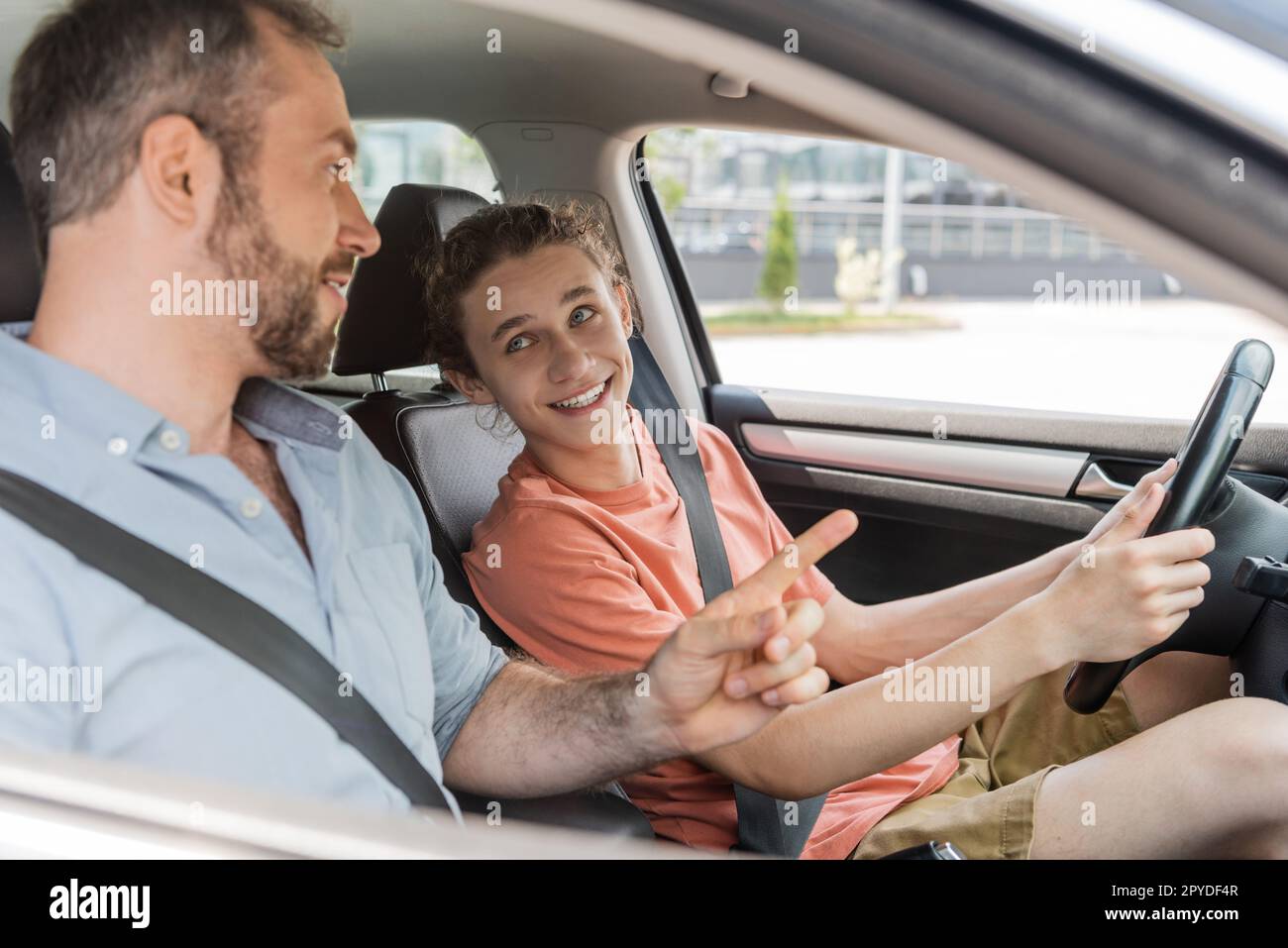 Ein glücklicher Teenager, der neben seinem Vater saß, während er das Autofahren lernte Stockfoto