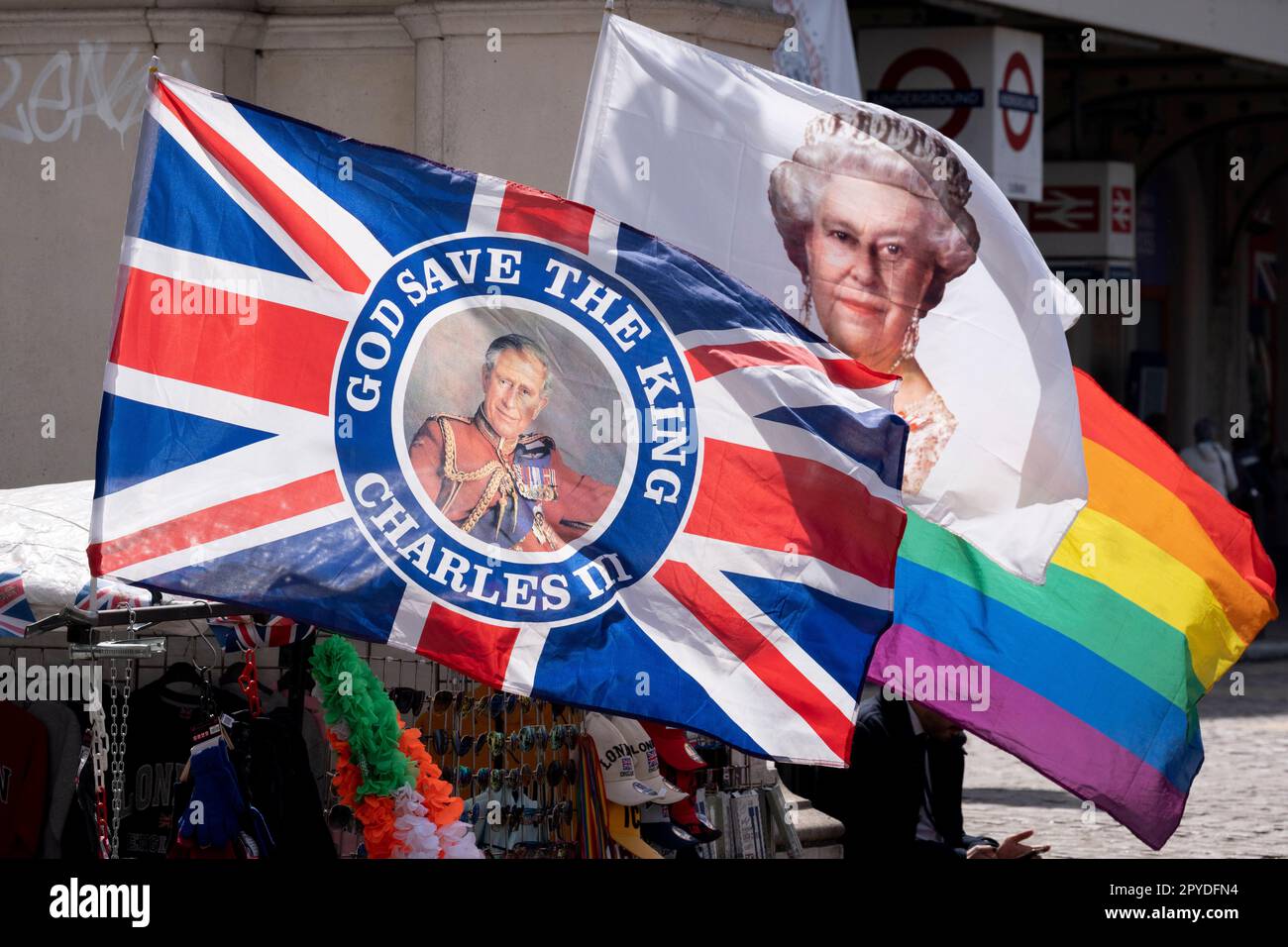 Nur vier Tage vor der Krönung von König Karl III., nach dem Tod seiner Mutter, Königin Elzabeth II. Im letzten Jahr, Flaggen Souvenirs an König Karl, seine verstorbene Mutter Königin Elizabeth und den LGBTQ-Regenbogen am Charing Cross, am 3. Mai 2023, in London, England. Stockfoto