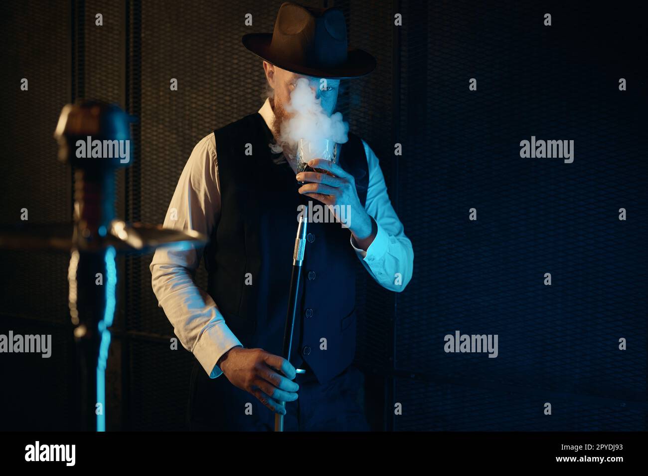 Vorderansicht eines ruhenden Mannes, der eine Wasserpfeife raucht, mit Neonbeleuchtung Stockfoto