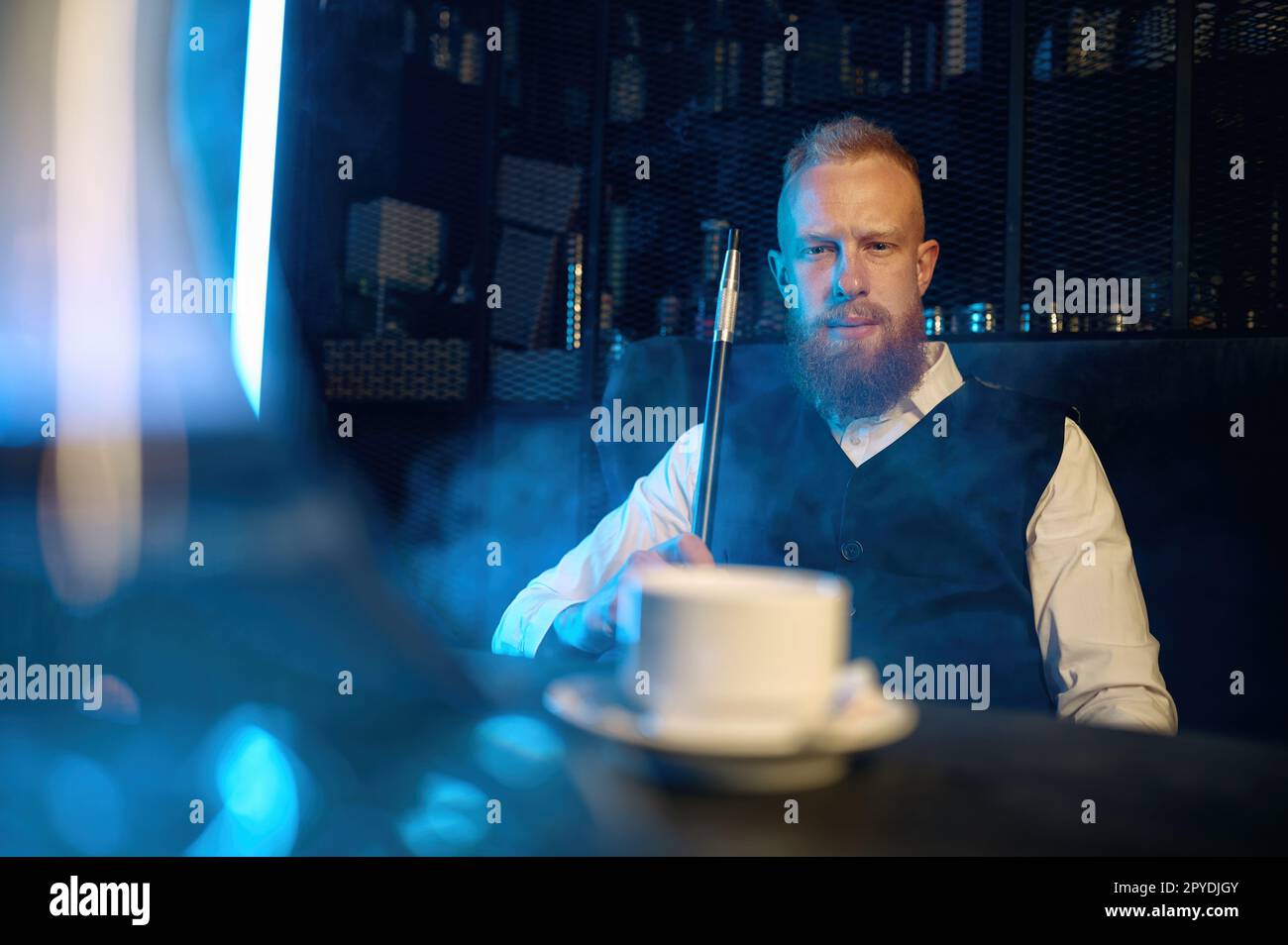 Ein gutaussehender bärtiger Mann, der eine Wasserpfeife raucht, während er in der Bar Kaffee trinkt Stockfoto