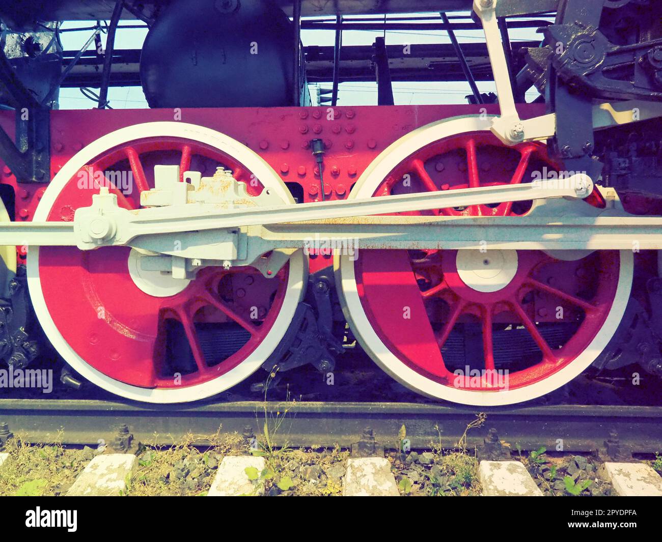 Retro-Räder einer Lokomotive oder eines Zuges aus nächster Nähe. Rote große Schwermetallräder mit Kolbenführungsmechanismen. Lokomotive des 19. - 20. Jahrhunderts mit einer Dampfmaschine. Retro-Style Stockfoto