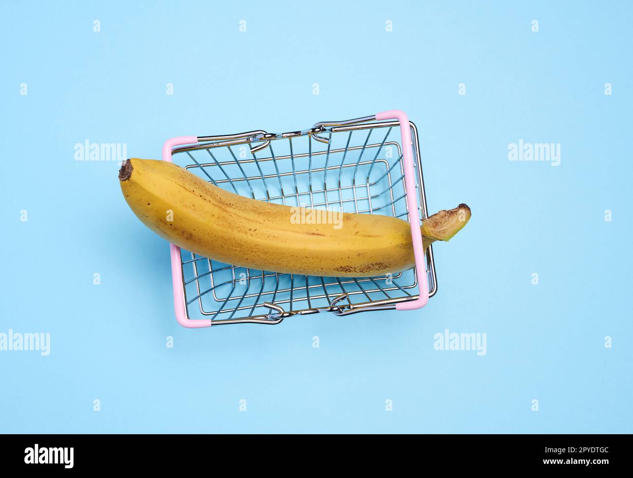 Eine reife Banane in einem Miniatur-Einkaufswagen auf blauem Hintergrund, die das Konzept des Verkaufs von Obst und Gemüse repräsentiert Stockfoto