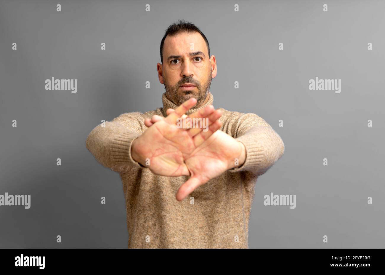 Ein hispanischer Mann, der über einem gelben Hintergrund steht und seine Arme und Handflächen mit einem negativen Zeichen kreuzt. Stockfoto