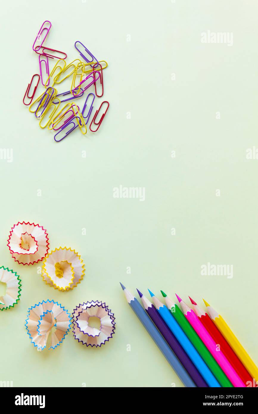 Die Buntstifte in den Ecken sind mit Spänen und farbigen Büroklammern auf hellgelbem Hintergrund für Büro- und Schularbeiten geschärft. Stockfoto