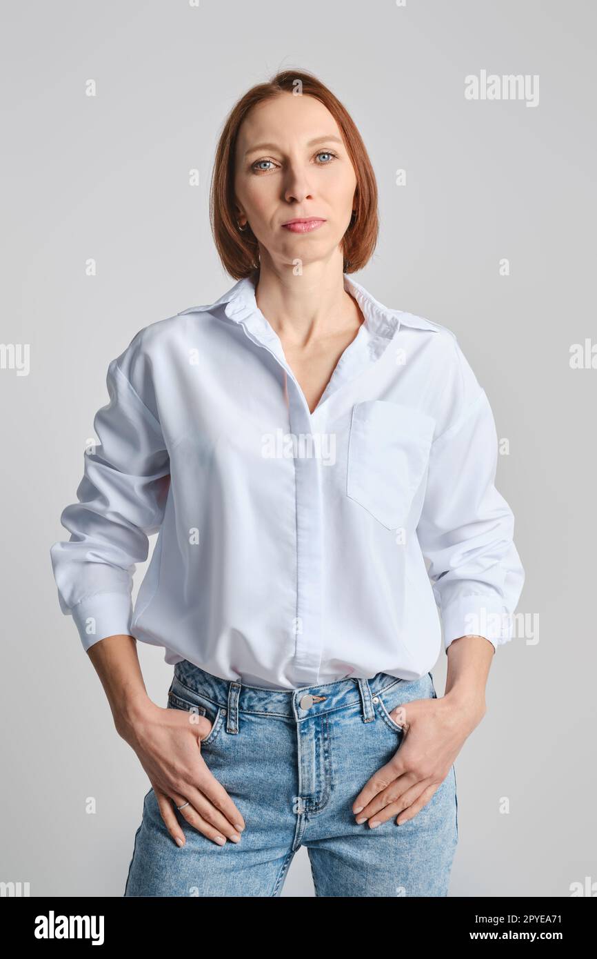 Eine Frau mittleren Alters im weißen Hemd und in blauen Jeans steckte Daumen in die Taschen Stockfoto