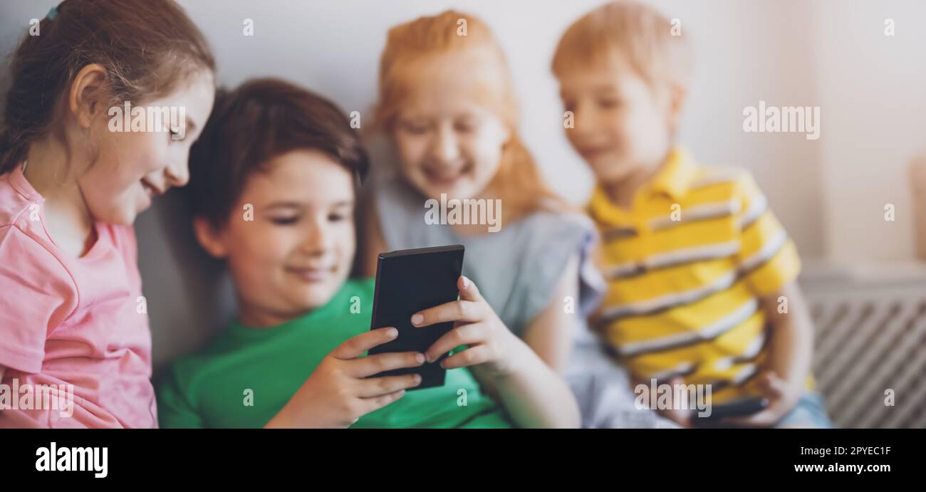 Gruppe von Kindern, die drinnen sitzen und im Smartphone schauen Stockfoto