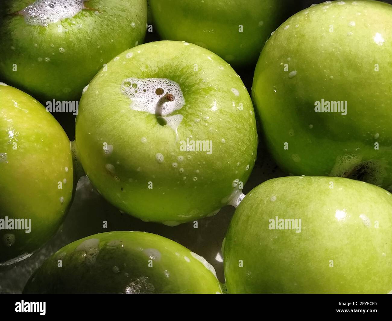 Grüne Äpfel, eingeseift und zum Abspülen mit Wasser bereit. Gute Hygiene beim Essen Stockfoto