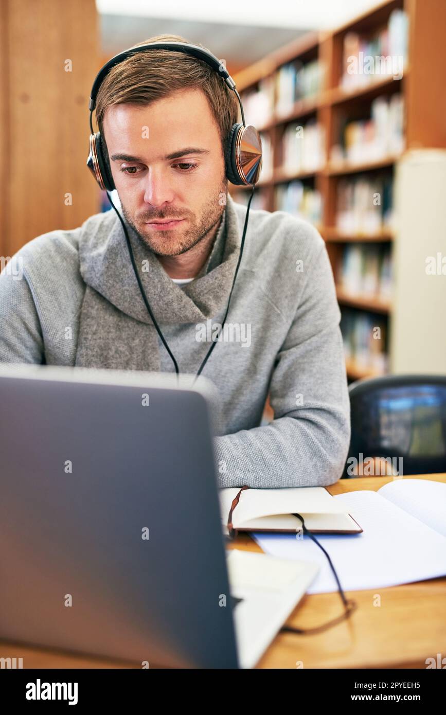 Er arbeitet hart daran, alle seine Aufgaben und Tests zu bestehen. Ein Student, der an einem Laptop in der Bibliothek auf dem Campus arbeitet. Stockfoto