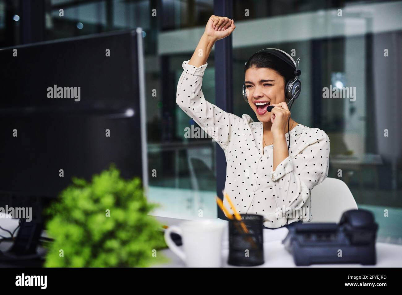 Ja, ein weiterer zufriedener Kunde. Eine attraktive junge Geschäftsfrau, die jubelt, während sie lange in einem Callcenter arbeitet. Stockfoto