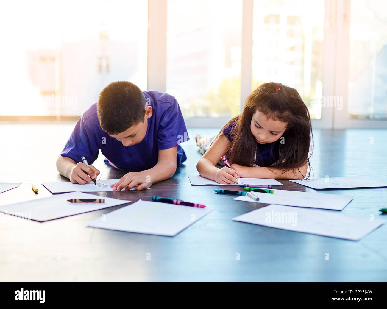 Lassen Sie sie immer frei kreativ sein. Zwei kleine Kinder, die auf dem Boden liegen und zu Hause Bilder in ihren Malbüchern ausmalen. Stockfoto