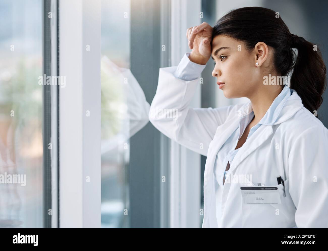 Das Problem des ärztlichen Burnouts wird immer häufiger. Eine junge Ärztin sieht gestresst aus, während sie in einem Krankenhaus am Fenster steht. Stockfoto