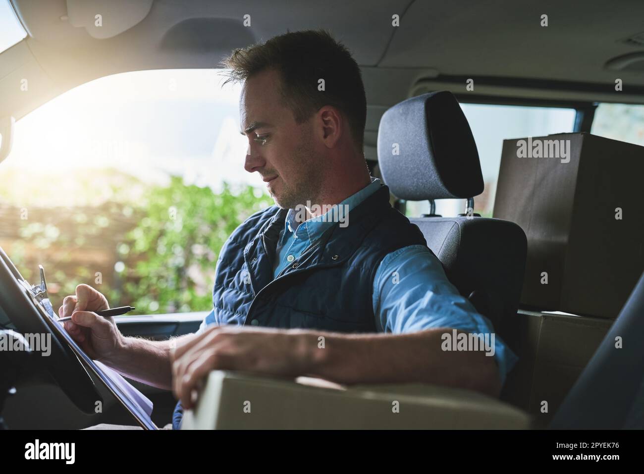 Ich organisiere seine nächsten Lieferstopps. Ein Kurier, der auf ein Klemmbrett schreibt, während er in einem Lieferwagen sitzt. Stockfoto