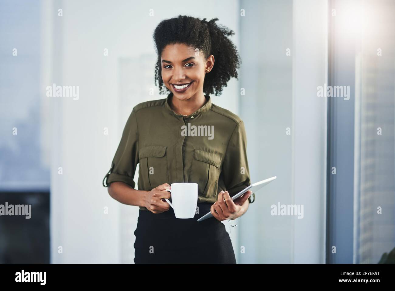 Ich beginne meinen Tag in einer positiven Stimmung. Porträt einer jungen Geschäftsfrau mit einer Tasse Kaffee und einem digitalen Tablet in ihrem Büro. Stockfoto