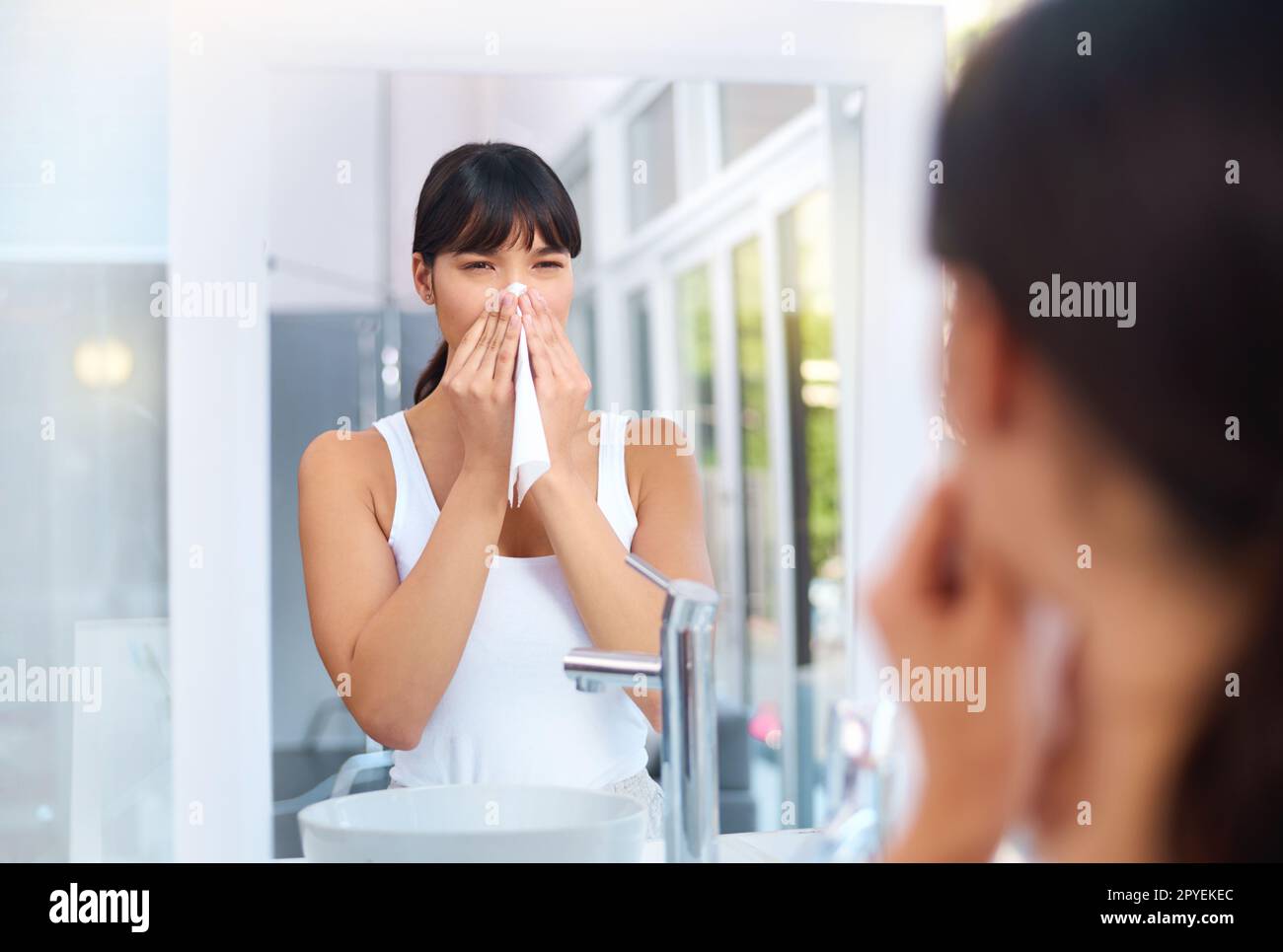 Putz dir die Nase. Eine fröhliche, attraktive junge Frau, die sich tagsüber die Nase bläst, während sie ihr Spiegelbild im Spiegel betrachtet. Stockfoto