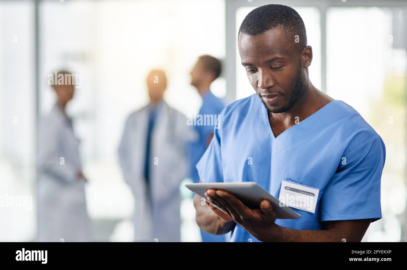 Verbesserung der medizinischen Diagnostik mit moderner Technologie. Ein junger Arzt, der ein digitales Tablet benutzt, mit seinen Kollegen im Hintergrund. Stockfoto