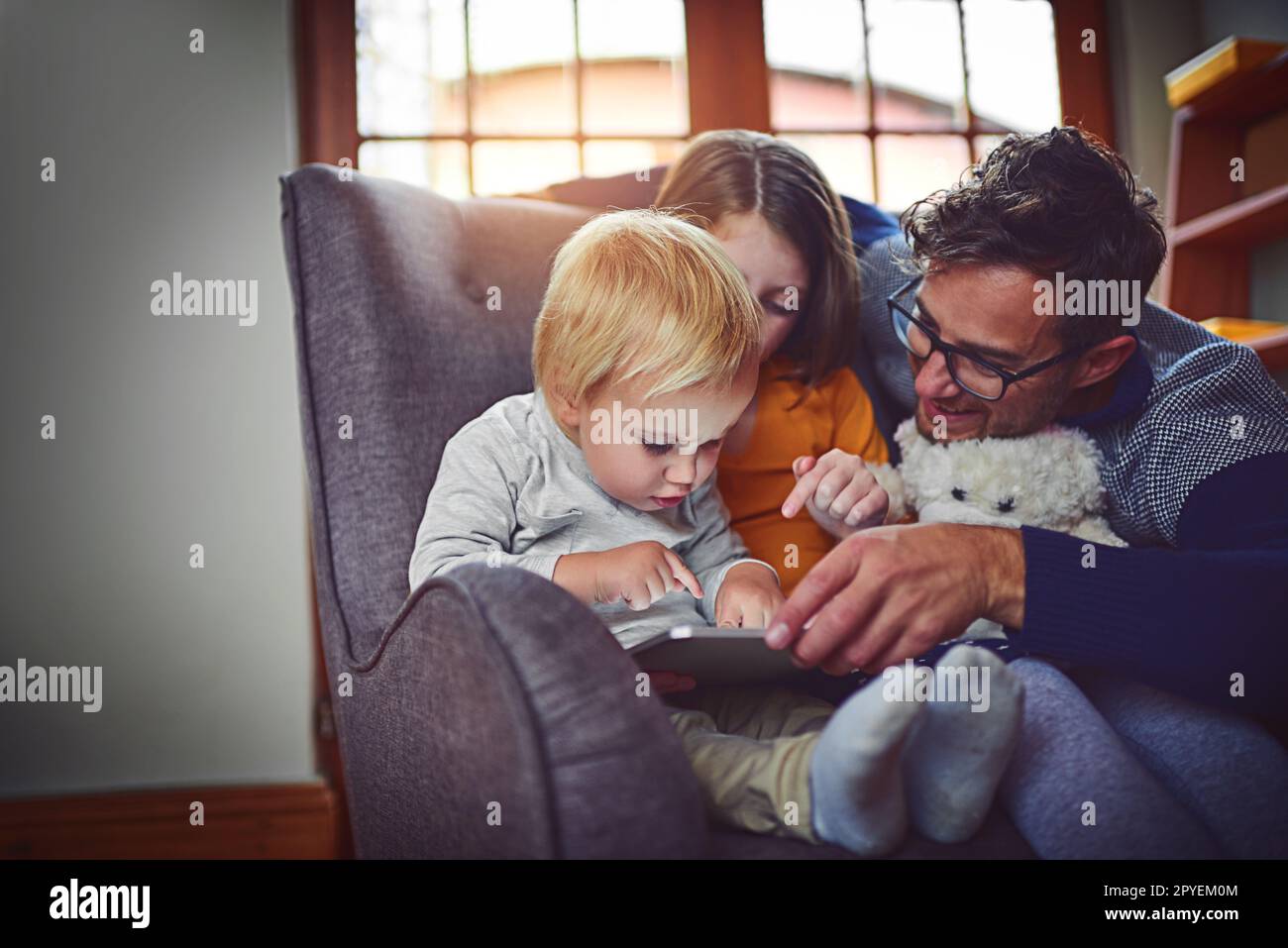 Fasziniert von den Wundern der Technik. Ein Vater, der ein digitales Tablet mit seinem kleinen Sohn und seiner Tochter zu Hause benutzt. Stockfoto