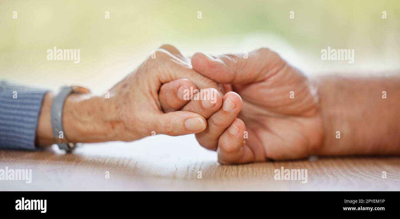 Ältere Ehepaare, Händchenhalten und Unterstützung für Komfort, Liebe oder Hilfe auf dem Tisch für Mitgefühl, Schmerz oder Sympathie. Seniorenmann, alte Frau und helfende Hand mit Einfühlungsvermögen, Vertrauen und Fürsorge zu Hause, um eine Beziehung aufzubauen Stockfoto
