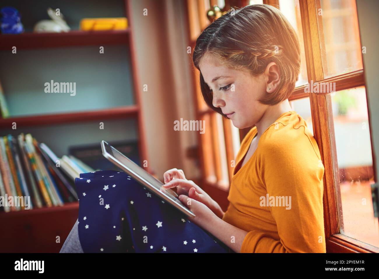 Sich in den Wundern der Technik zu verirren. Ein kleines Mädchen, das zu Hause ein digitales Tablet benutzt. Stockfoto