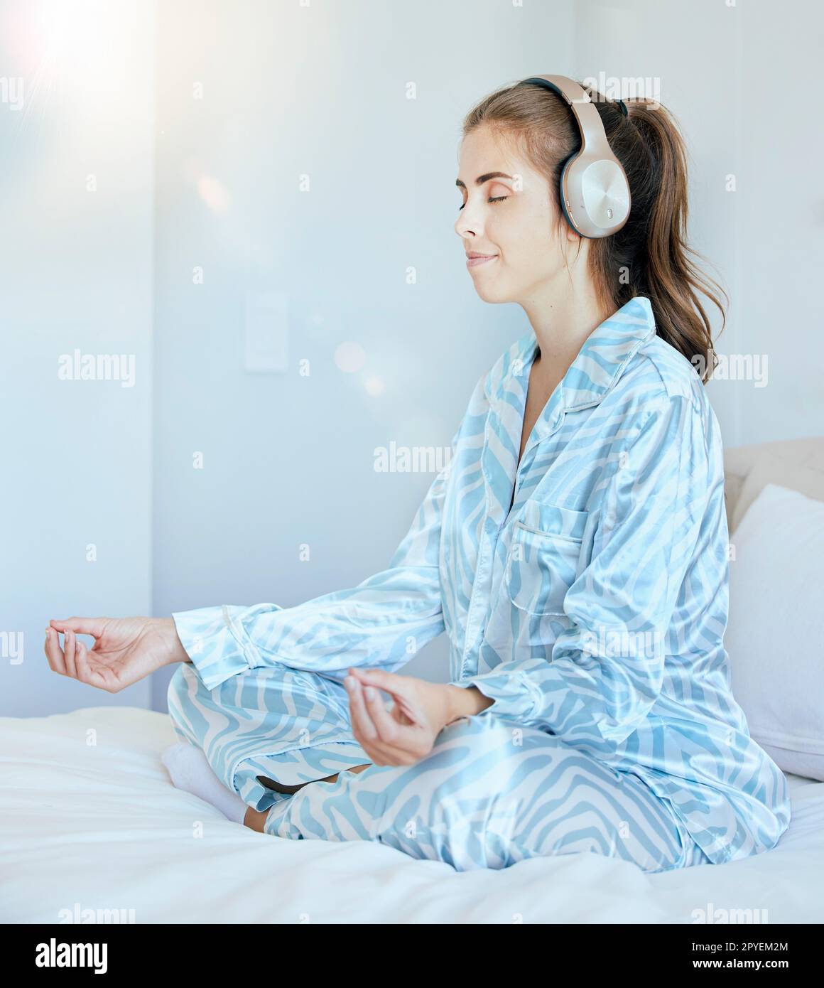 Yoga, Meditation oder Zen Woman im Schlafzimmer mit Kopfhörern, die entspannendes Radio streamen, ruhige Musik oder Podcast. Frieden, geistige Gesundheit oder spirituelles Mädchen in Lotus posieren, um für Achtsamkeit oder Wellness zu meditieren Stockfoto
