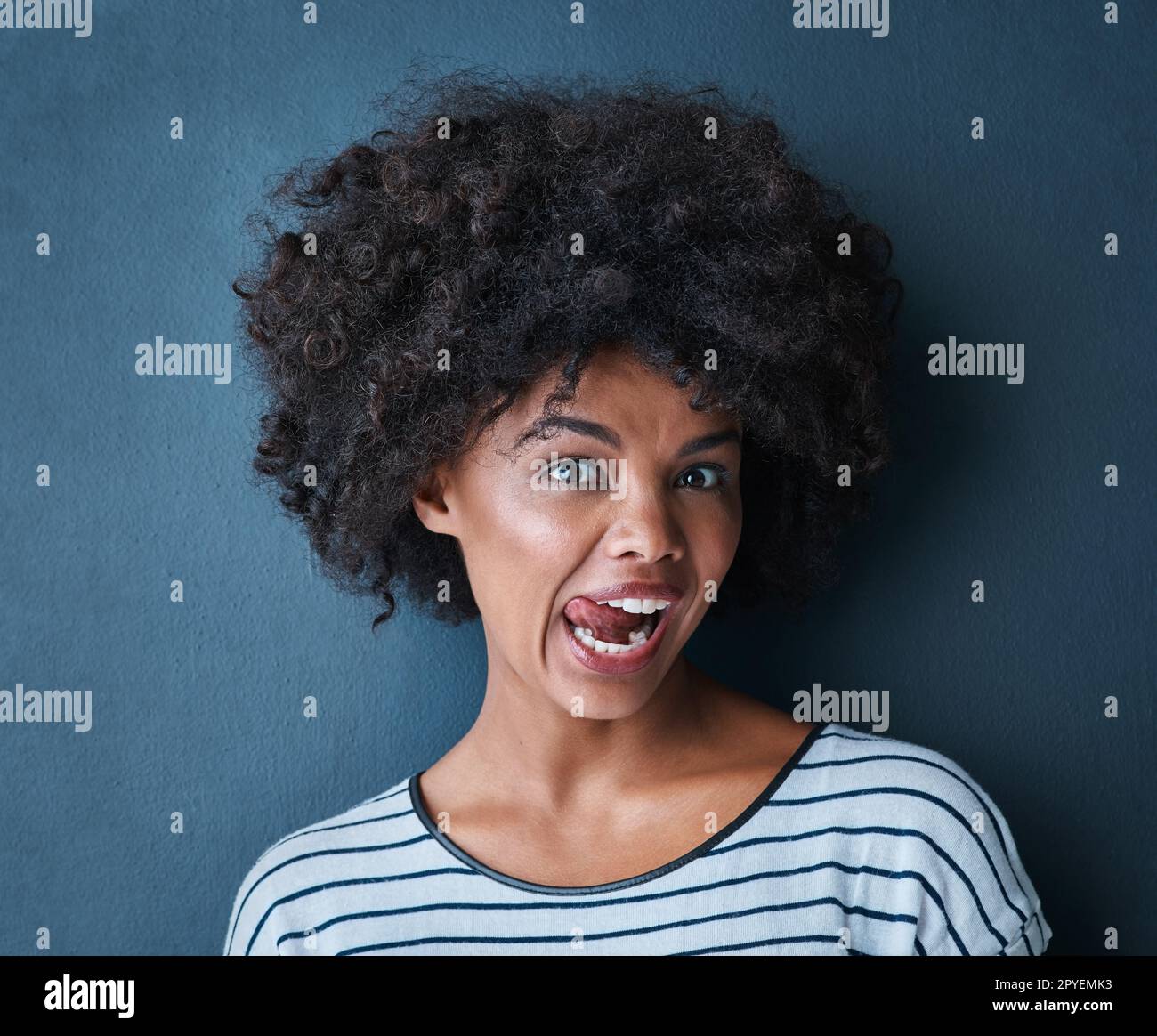 Manchmal muss man einfach die Dummheit rauslassen. Studio-Porträt einer attraktiven jungen Frau, die verspielt ihre Zunge vor blauem Hintergrund herausstreckt. Stockfoto