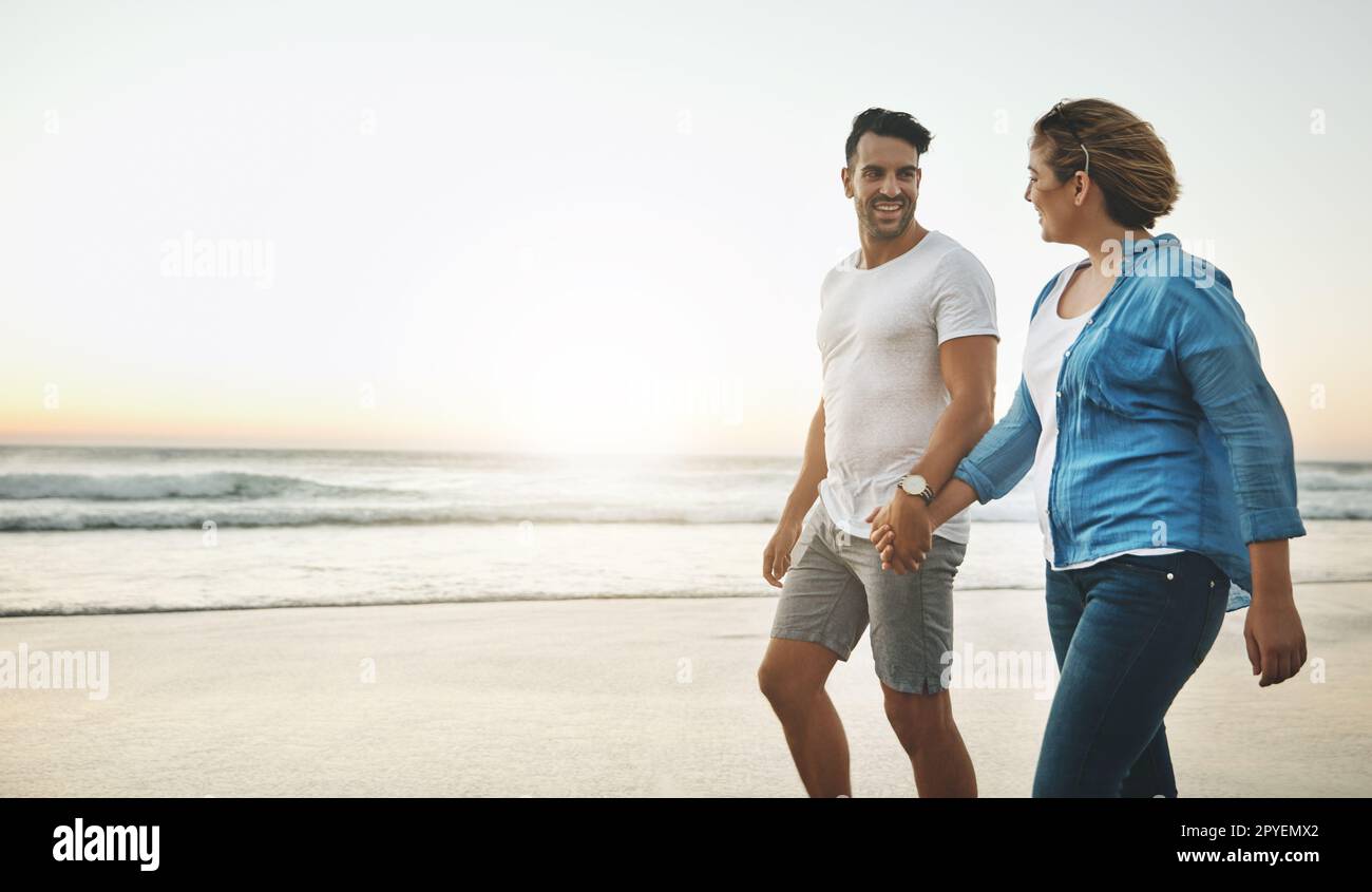 Hand in Hand bis ans Ende der Zeit. Ein liebevolles Paar, das Hand in Hand am Strand spaziert. Stockfoto