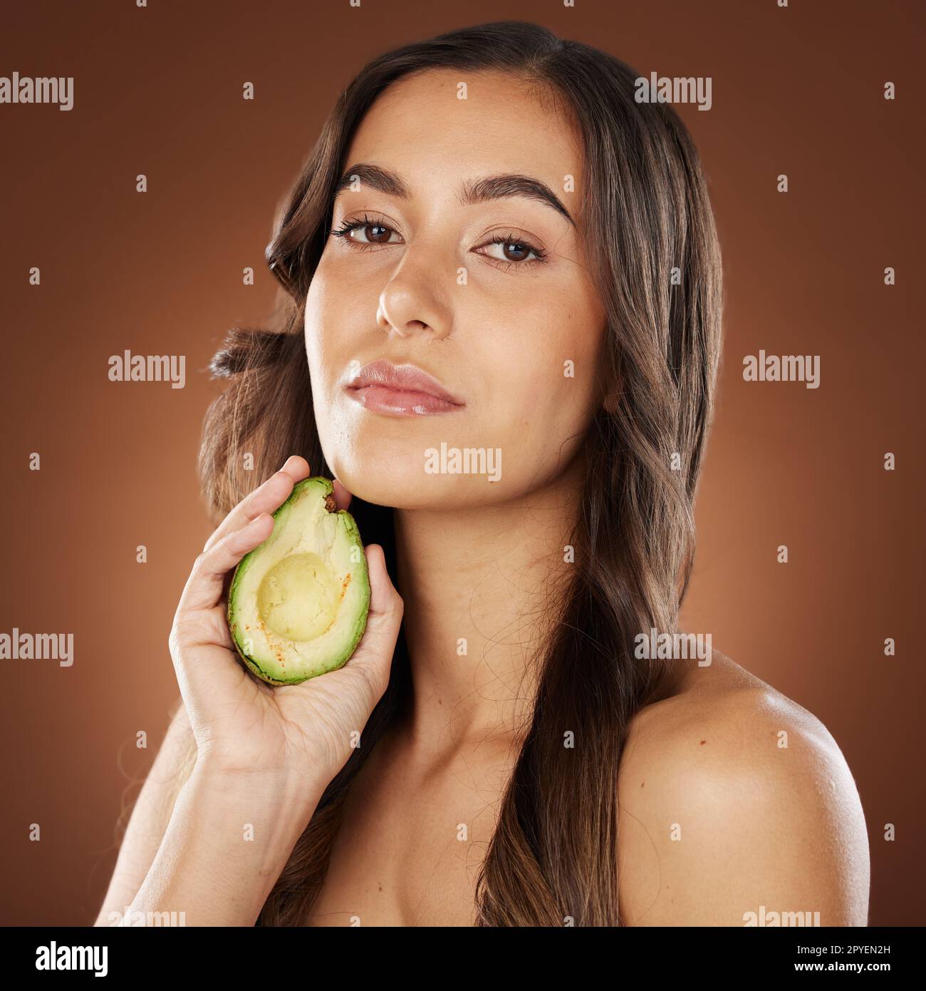 Gesichtsporträt, Hautpflege und Frau mit Avocado im Studio auf braunem Hintergrund. Schönheit, organische Kosmetik und junge weibliche Modell mit Obst, Produkt oder Nahrung für gesunde Ernährung, Ernährung und Vitamin c.. Stockfoto