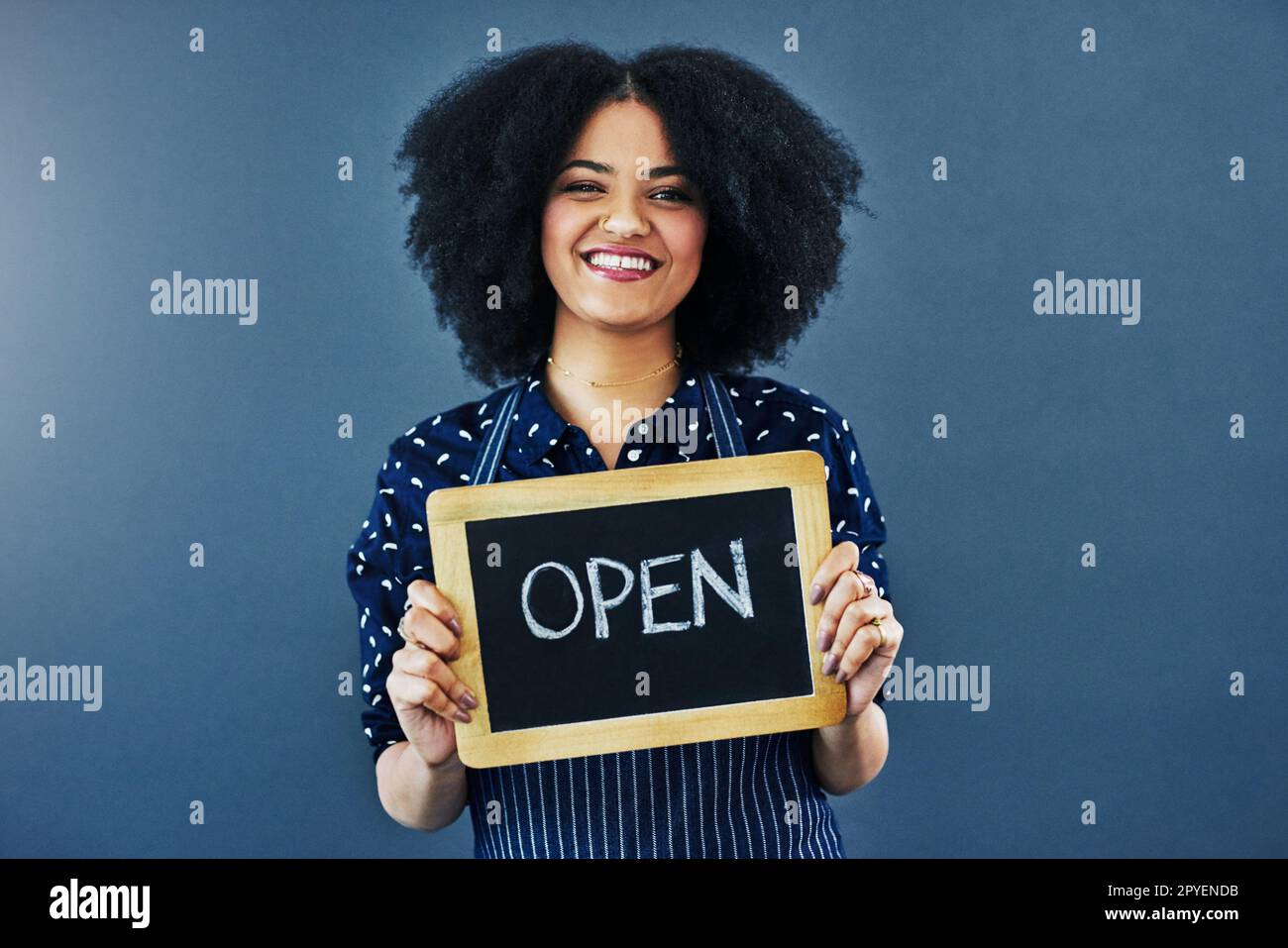 Herzlich Willkommen. für bestehende und neue Kunden Studiofoto einer jungen Frau, die eine Tafel hält, mit dem Wort offen auf blauem Hintergrund. Stockfoto