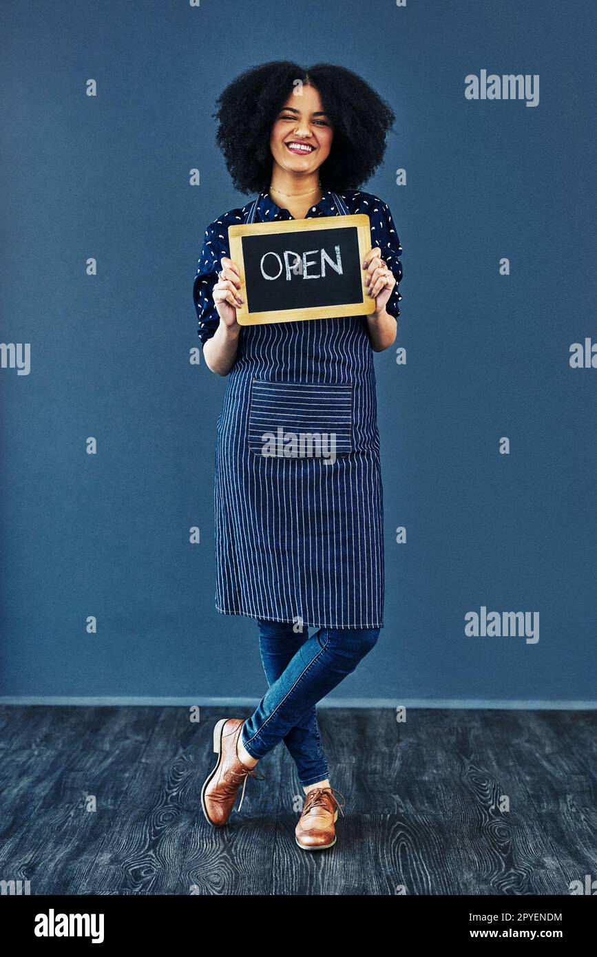 Alle Kunden Herzlich Willkommen. Studiofoto einer jungen Frau, die eine Tafel hält, mit dem Wort offen auf blauem Hintergrund. Stockfoto