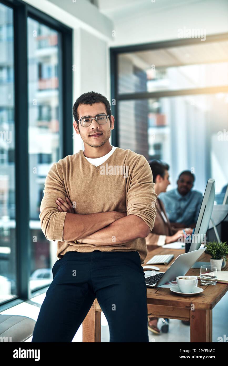 Niemand wird meiner Vision im Weg stehen. Ein Designer, der im Büro mit Kollegen posiert, die im Hintergrund verschwommen sind. Stockfoto