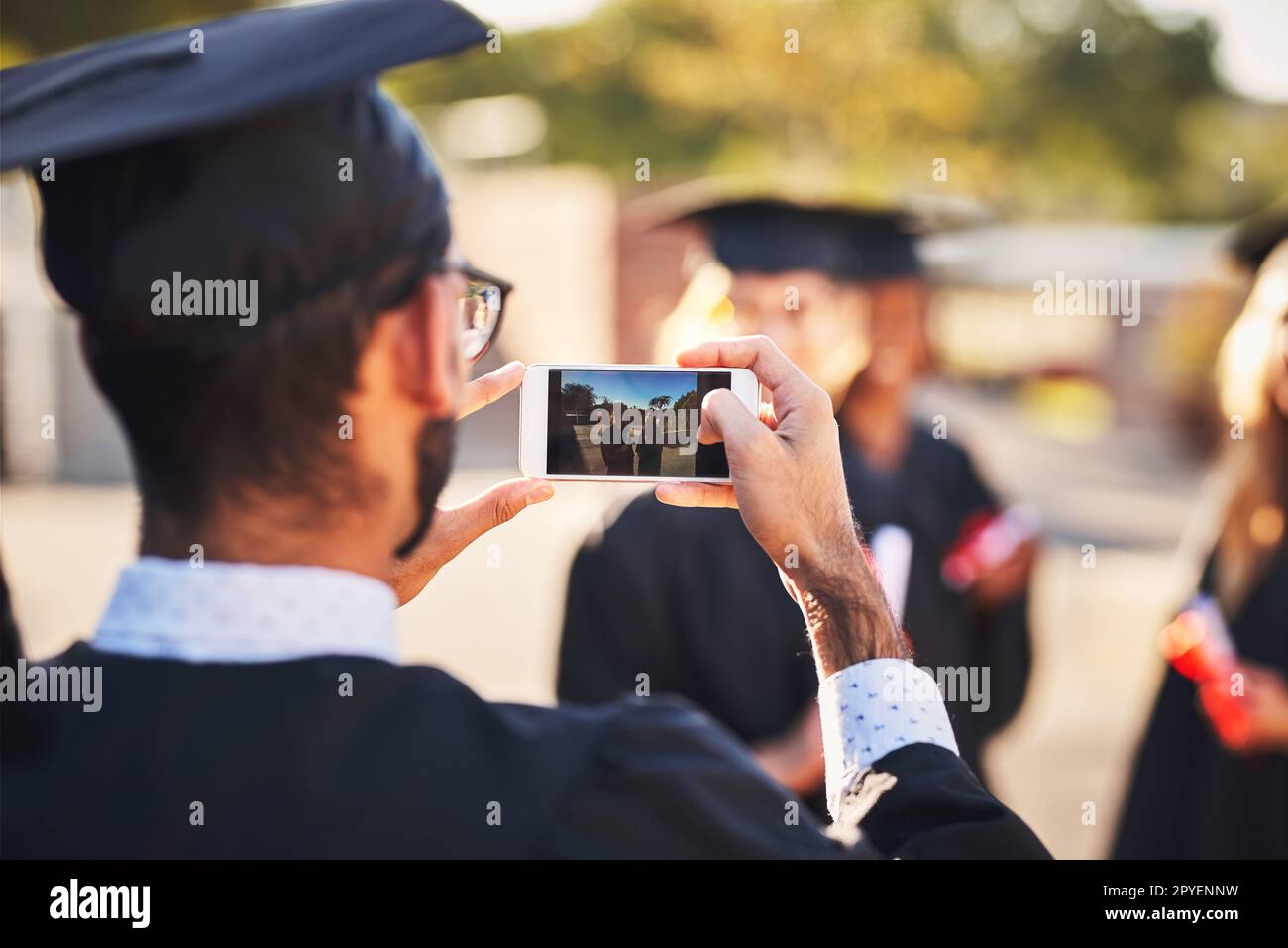 Ein Meilenstein ohne Erinnerungen. Eine Gruppe von Schülern, die am Abschlusstag mit einem Mobiltelefon Fotos machen. Stockfoto