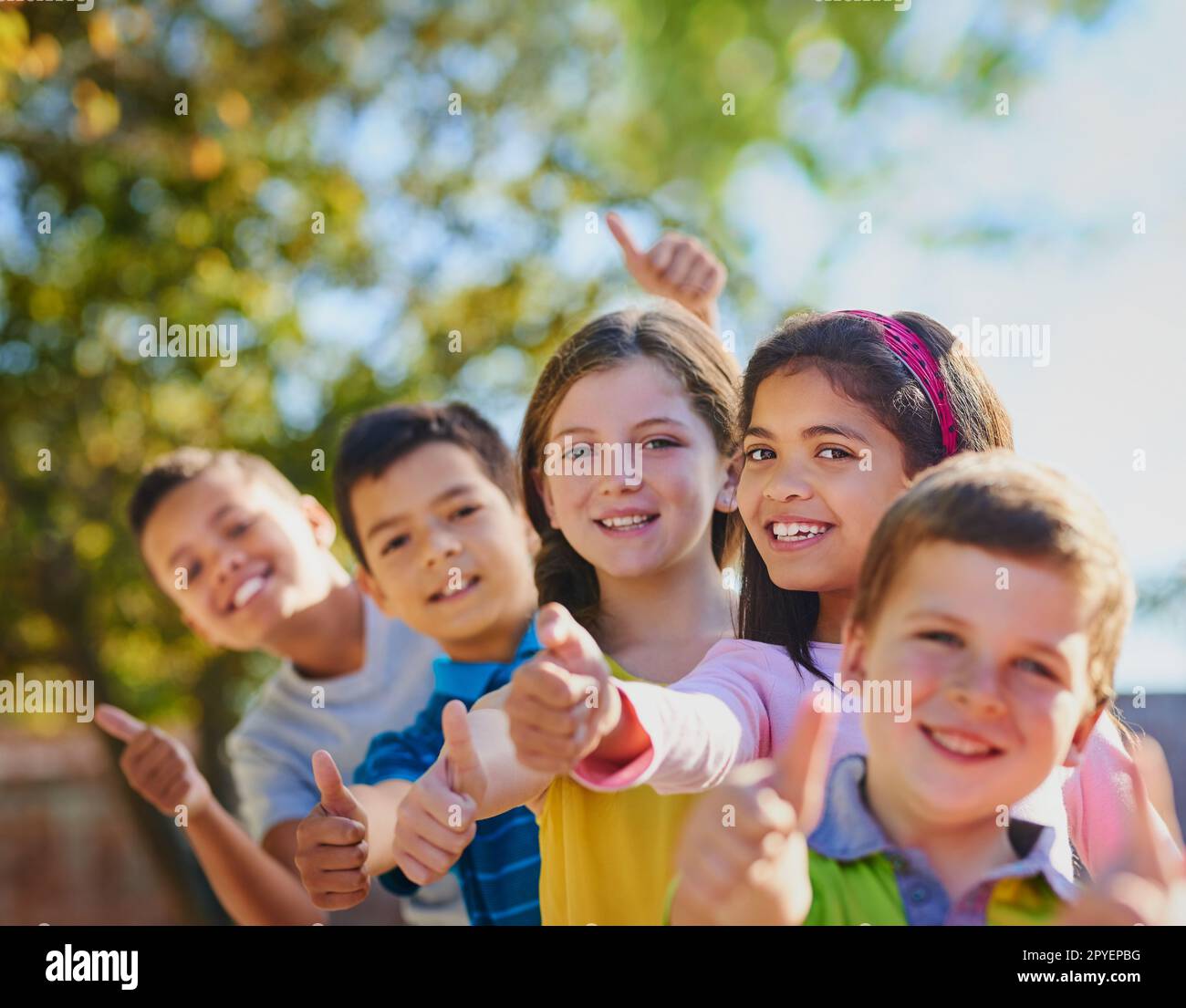 Daumen hoch, um Spaß zu haben. Eine vielfältige Gruppe von Kindern, die draußen Daumen nach oben zeigen. Stockfoto