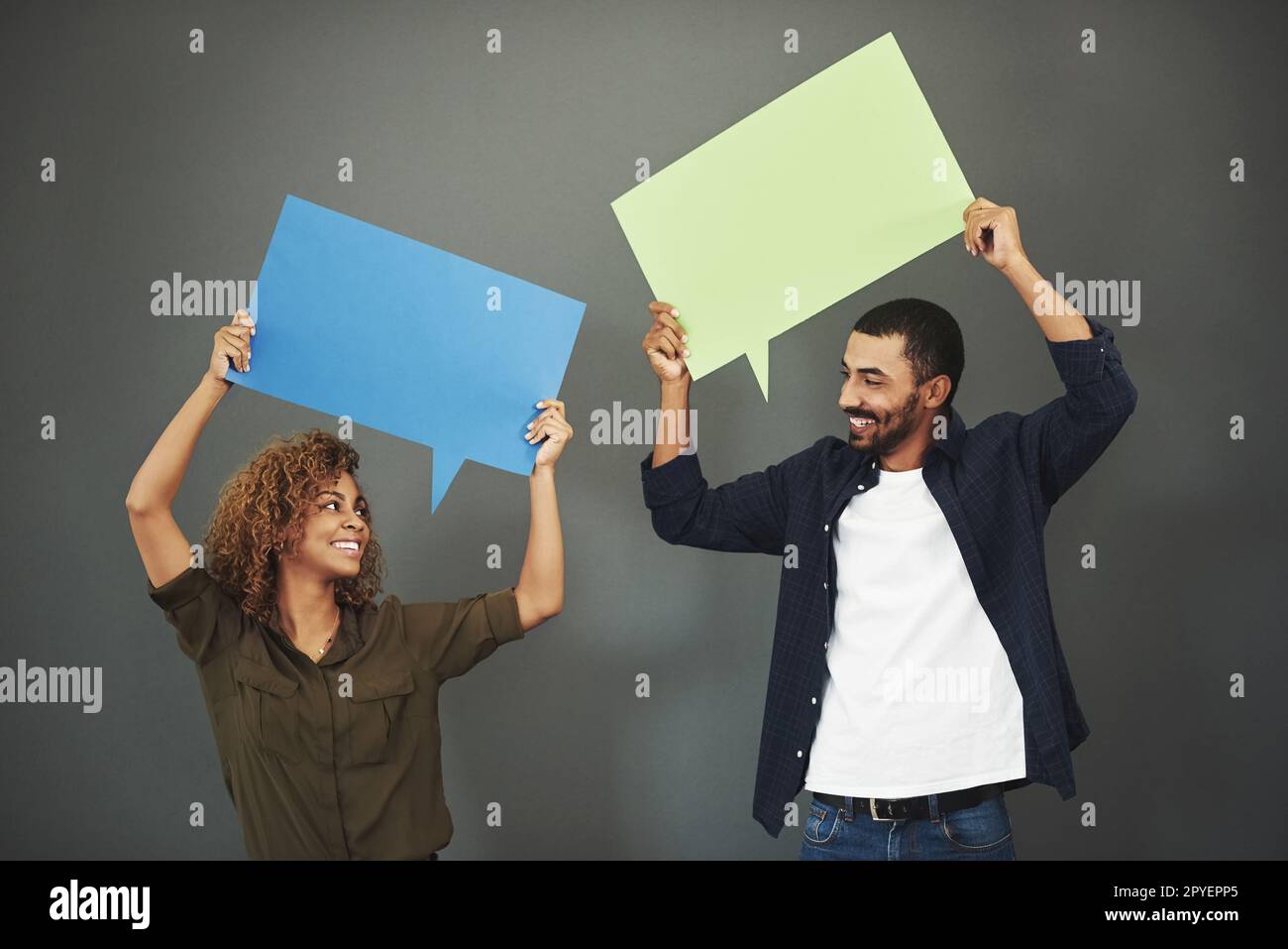 Gemeinsam können wir mehr sagen und mehr tun. Studioaufnahme eines jungen Ehepaars mit Sprachblasen vor grauem Hintergrund. Stockfoto