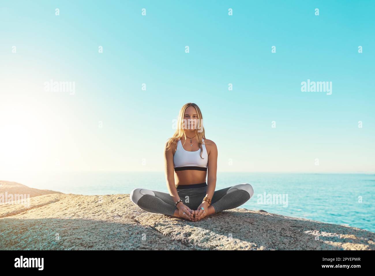 Yoga ist der Grund, warum ich ein glücklicheres Leben führe. Eine junge Frau, die am Strand Yoga macht. Stockfoto