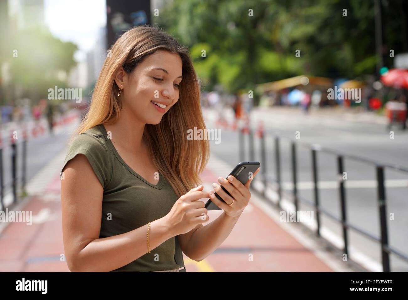 Lächelndes, wunderschönes Mädchen auf der Paulista Avenue mit Smartphone, Sao Paulo, Brasilien Stockfoto