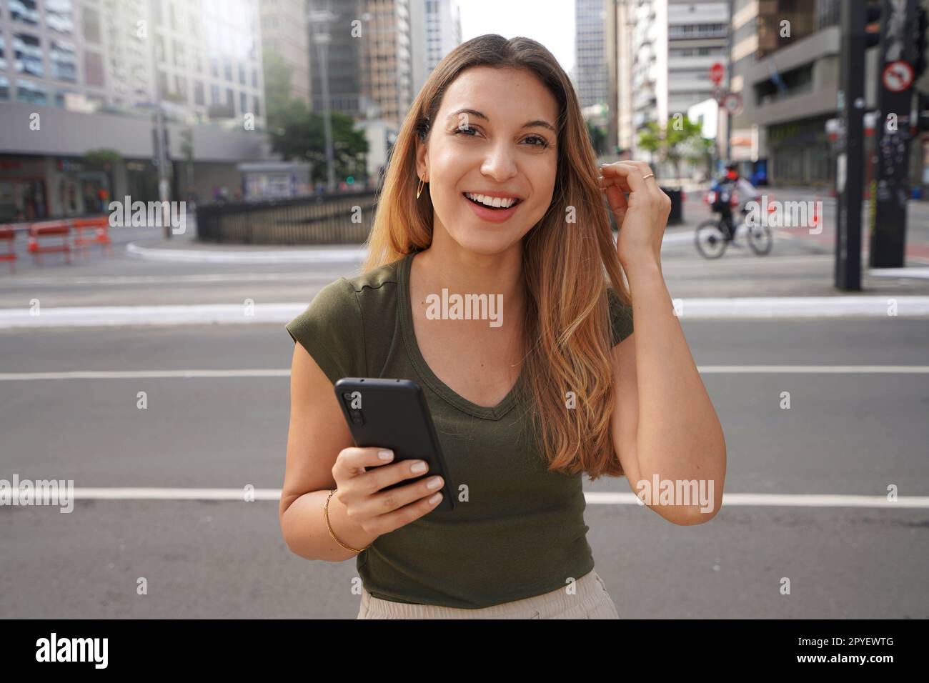 Authentische Menschen im Freien. Selbstbewusstes Mädchen mit Handy, das in der leeren Metropole in die Kamera schaut, am Morgen im Sommer. Stockfoto
