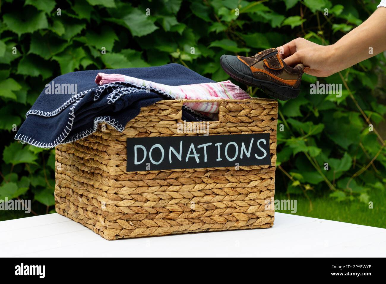 Hand, die ein Kinderschuhe in eine Box für Spenden auf einem grünen Hintergrund. Wohltätigkeitskonzept und Spendenkonzept. Speicherplatz kopieren. Stockfoto