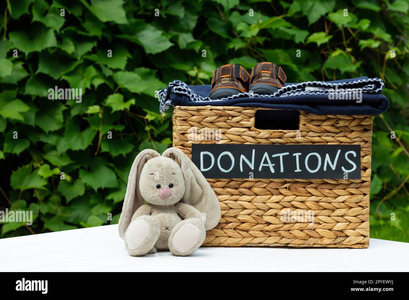 Spendenbox mit Kinderschuhen und Spielzeughase auf grünem Hintergrund. Wohltätigkeitskonzept und Spendenkonzept. Speicherplatz kopieren. Stockfoto