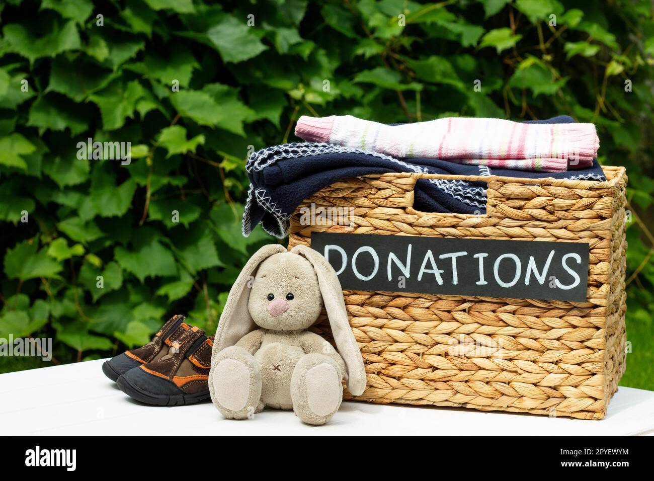 Spendenbox mit Kinderschuhen und Spielzeughase auf grünem Hintergrund. Wohltätigkeitskonzept und Spendenkonzept. Speicherplatz kopieren. Stockfoto
