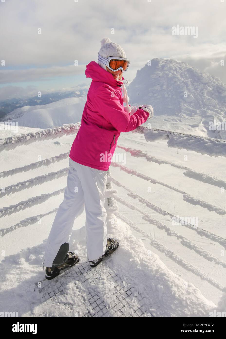 Junge Frau in Rosa ski Jacke, Hosen, Schuhe, Mütze und Handschuhe, lehnte sich auf Schnee bedeckten Rampe, lächelnd. Stockfoto