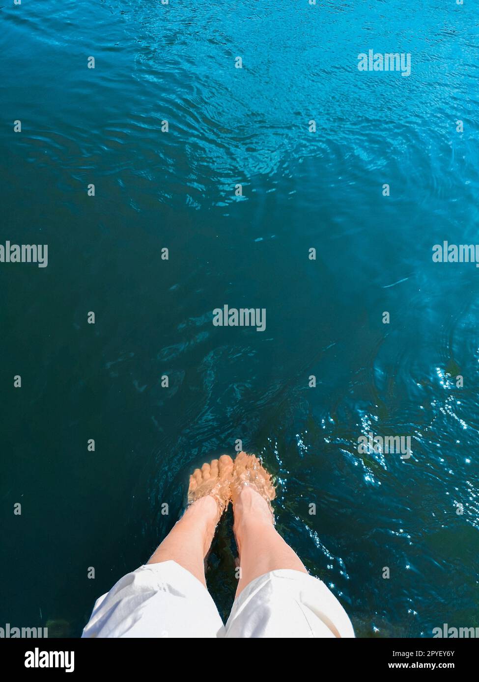 Eine Frau senkte ihre Füße in türkisfarbenes Meerwasser Stockfoto