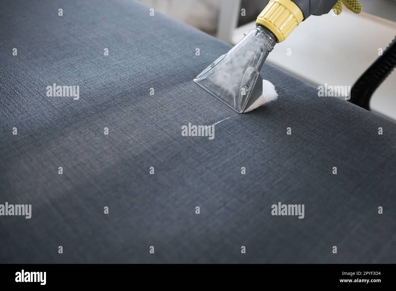 Die Hand des Reinigers man im Schutzhandschuh-Reinigungssofa mit professioneller Absaugmethode. Im Frühling wird regelmäßig aufgeräumt. Das Konzept der gewerblichen Reinigungsfirma Stockfoto