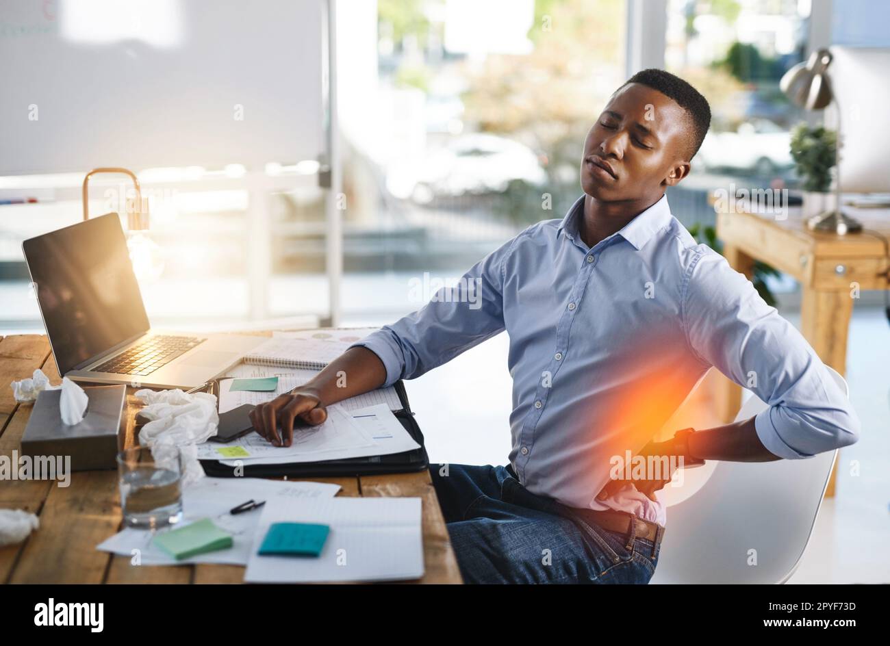 Ich arbeite ein bisschen zu hart. Ein junger Geschäftsmann, der Rückenschmerzen hat, während er versucht, im Büro zu arbeiten. Stockfoto