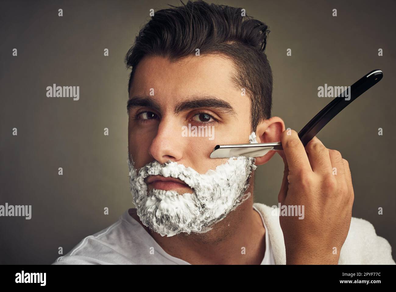 Achten Sie darauf, dass sie ordentlich und getrimmt ist. Ein hübscher junger Mann, der sich mit einem Rasierer rasiert. Stockfoto