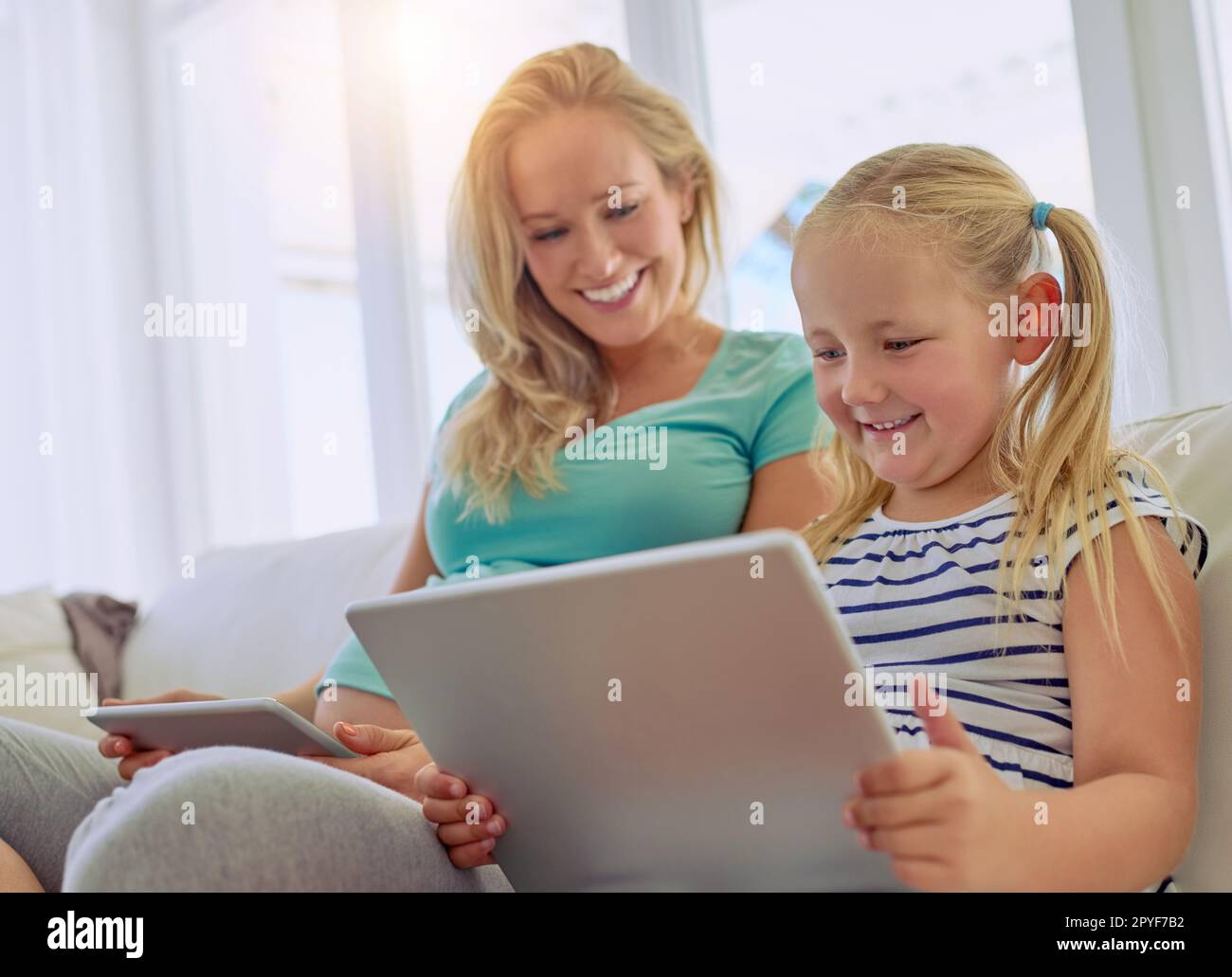 Ich recherchiere darüber, eine große Schwester zu werden. Eine schwangere Frau und ihre kleine Tochter, die zu Hause digitale Tablets verwenden. Stockfoto