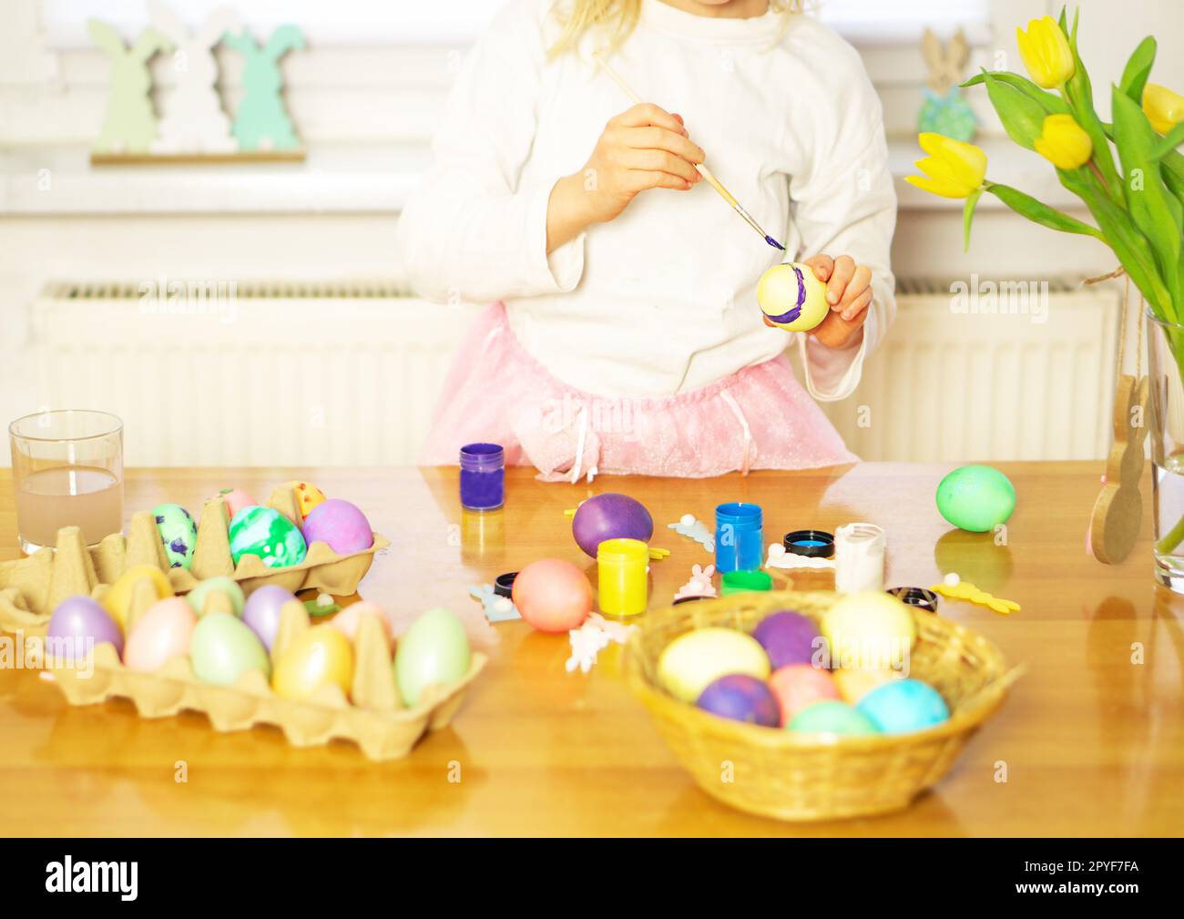 Ein kleines Mädchen, das zu Ostern Eier auf dem Holztisch malt. Vorbereitung für Ostern. Stockfoto